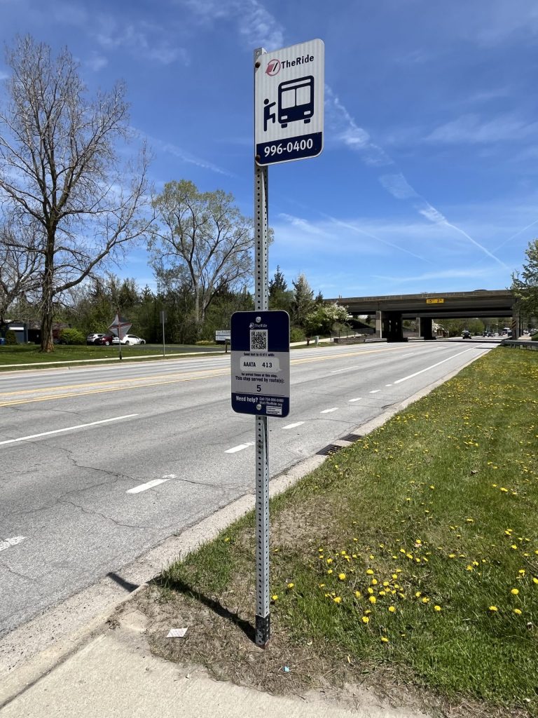 TheRide bus stop sign for route 5 beside Packard Road, with the US-23 overpass in the distance.